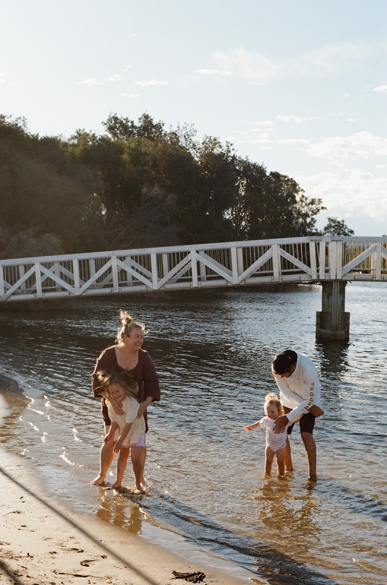 A family paddling in the shallows beside the walkway bridge at Gerroa