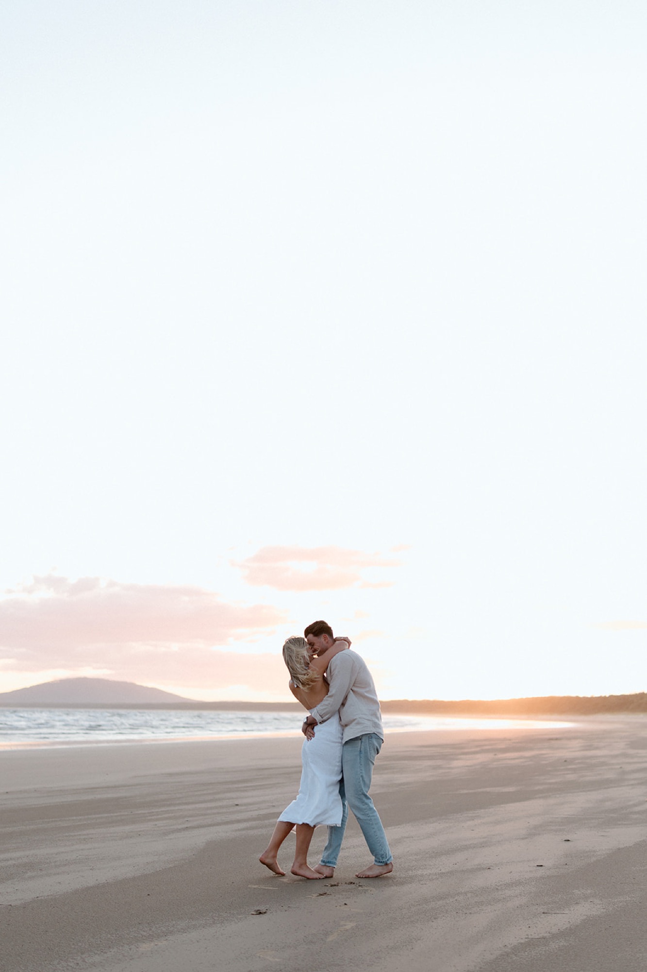 A couple embracing on the beach under a pink sunset sky