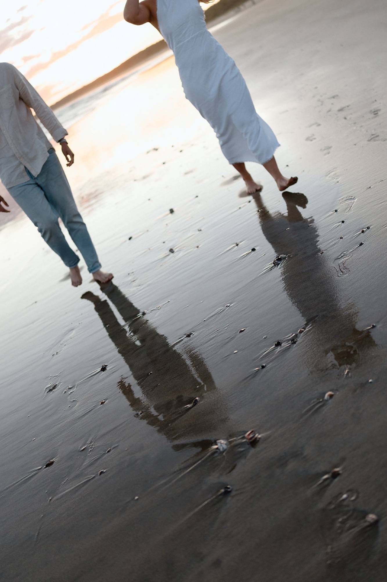 A couple reflected in the wet sand as they walk along the shore