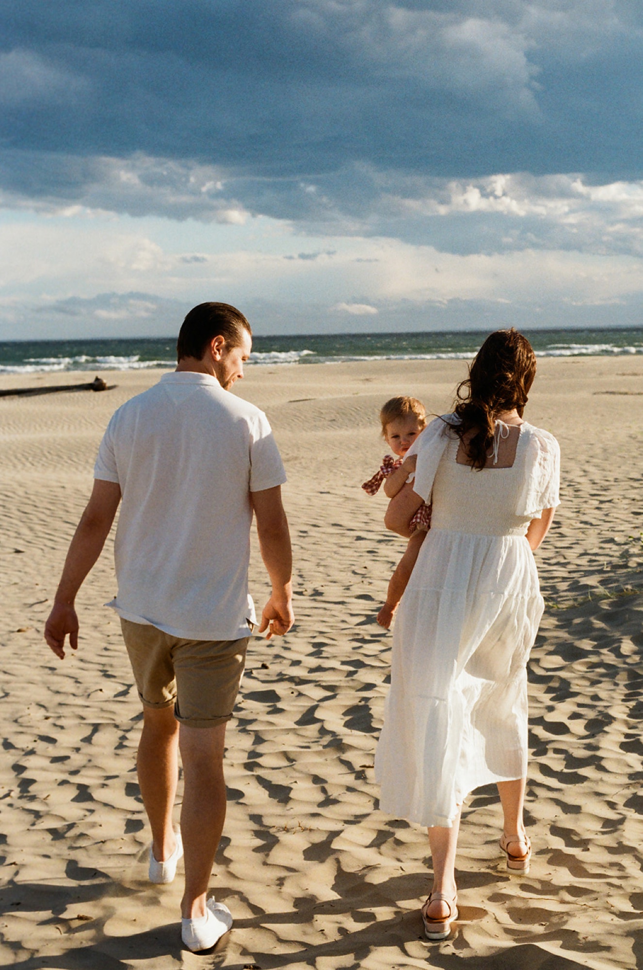 A mum and dad walking across the sand carrying their toddler