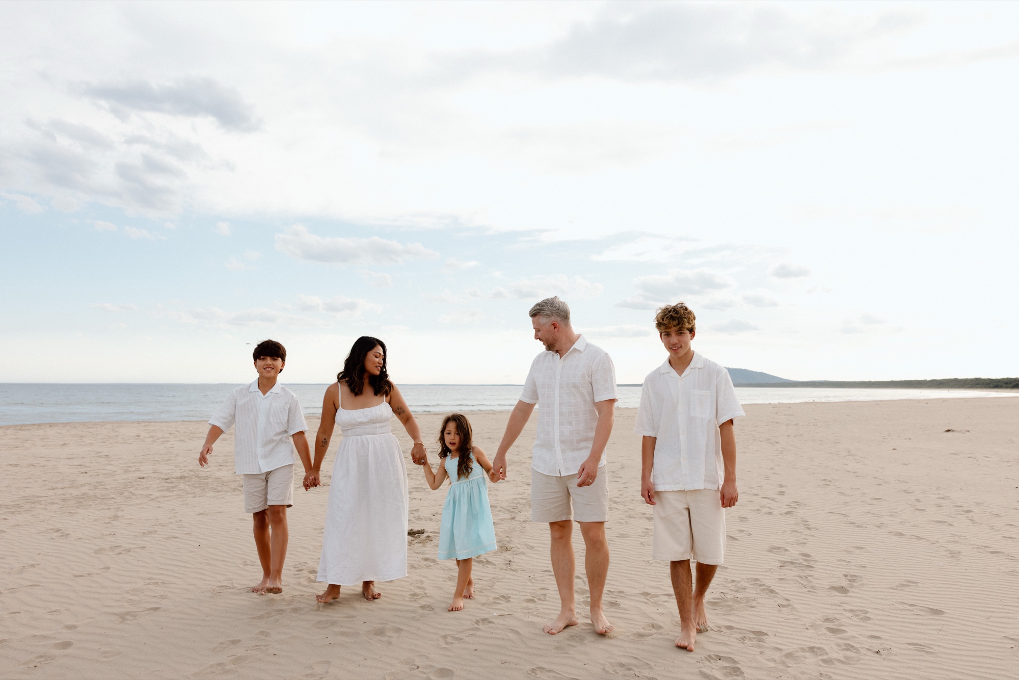 A family of five walking hand in hand along the beach